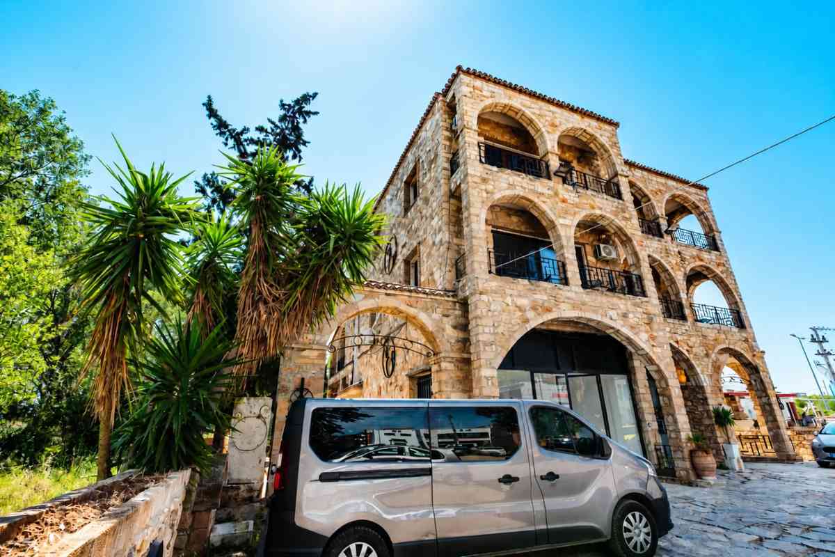 Πέτρινη τοξωτή πρόσοψη του Stone Palace Hotel με φοίνικες και εξωτερικό χώρο