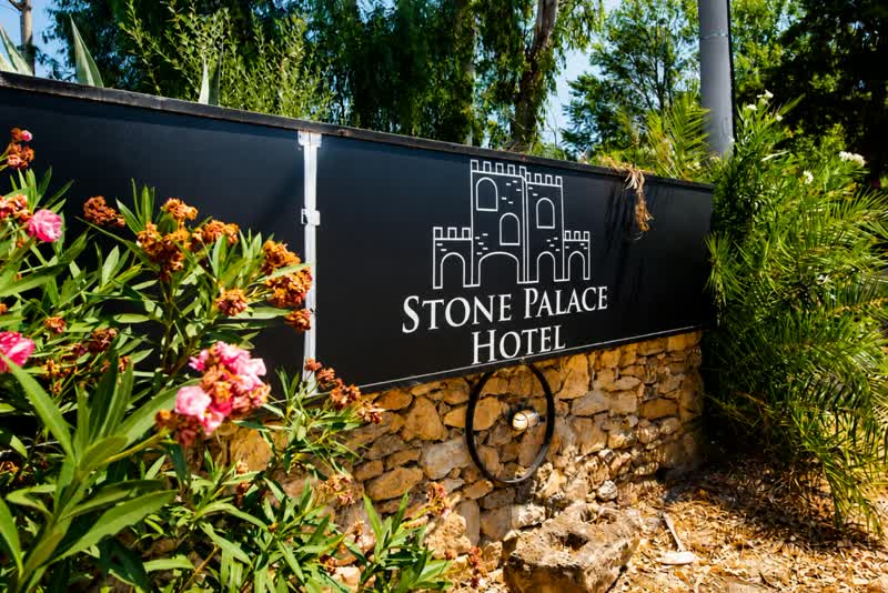 Η πινακίδα εισόδου του Stone Palace Hotel ανάμεσα σε φυτά